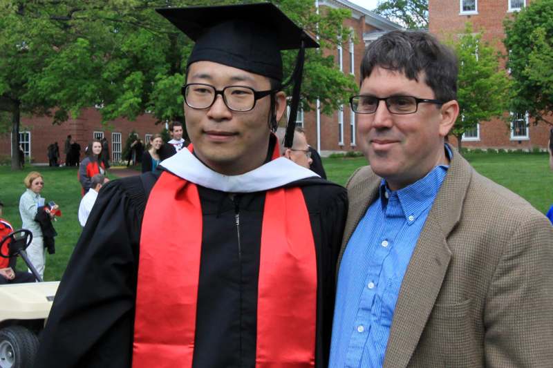 a man in a graduation cap and gown standing next to a man in a brown jacket