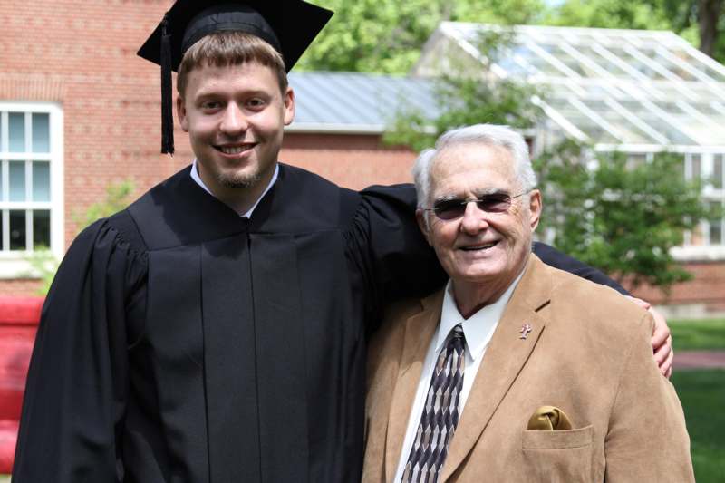 a man in a graduation gown and cap standing next to an old man