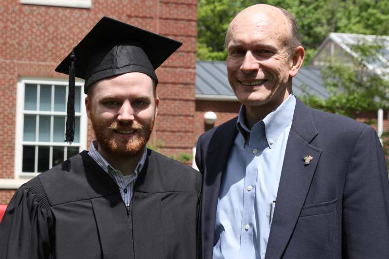 a man in a graduation cap and gown standing next to a man in a suit