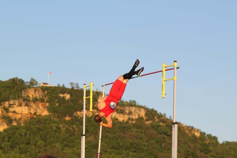 a man in red jumps over a bar