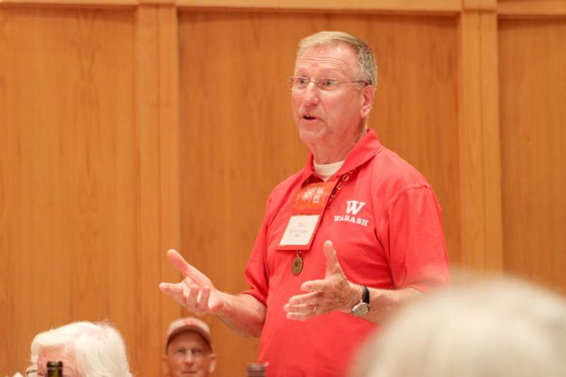 a man in a red shirt speaking to a group of people