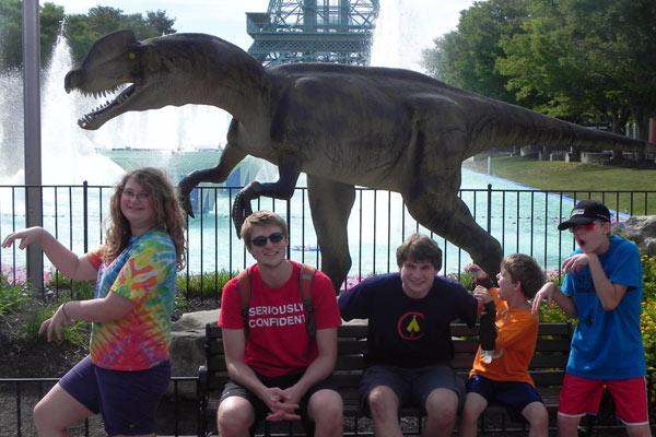 a group of people sitting on a bench in front of a statue of a dinosaur