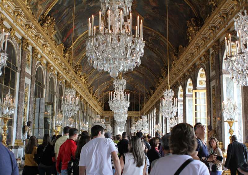 a group of people in a room with chandeliers with Palace of Versailles in the background