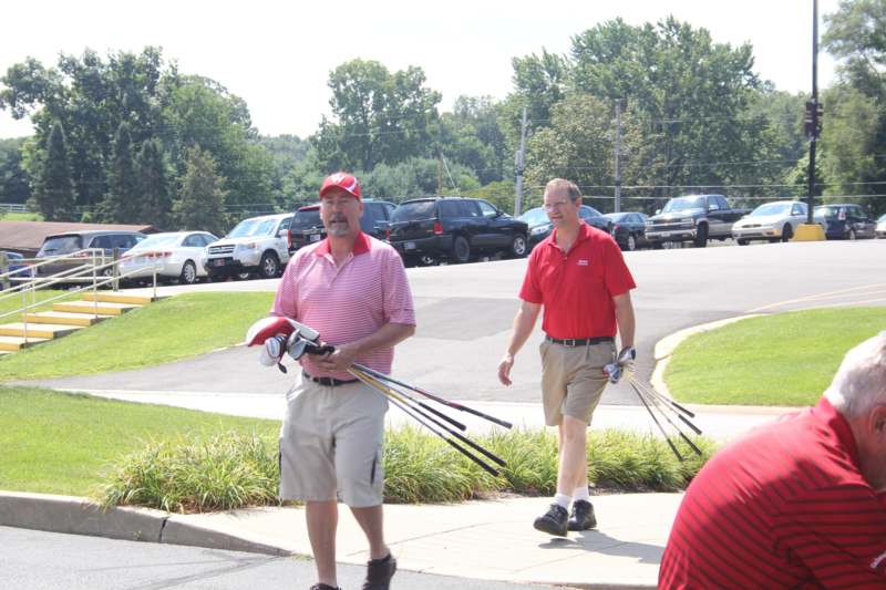a group of men walking on a sidewalk with golf clubs