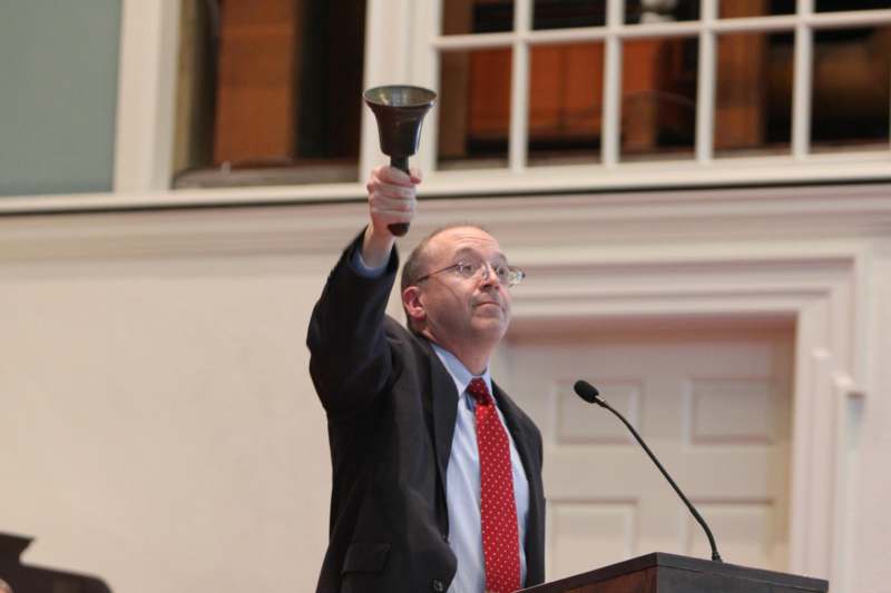a man holding a bell up at a podium