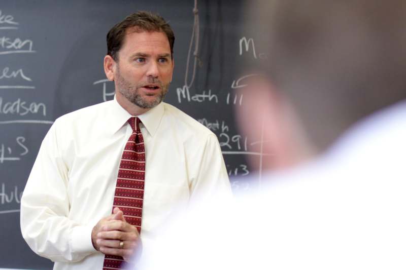 a man in a white shirt and tie talking to a man in a blackboard