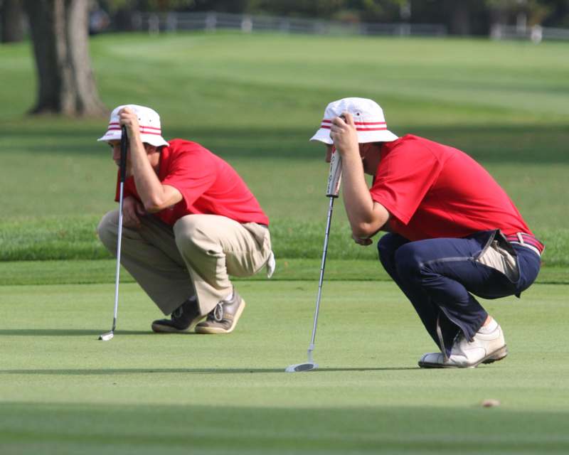 a couple of men in red shirts and white hats on a golf course
