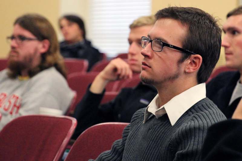 a man in a grey sweater sitting in a lecture hall