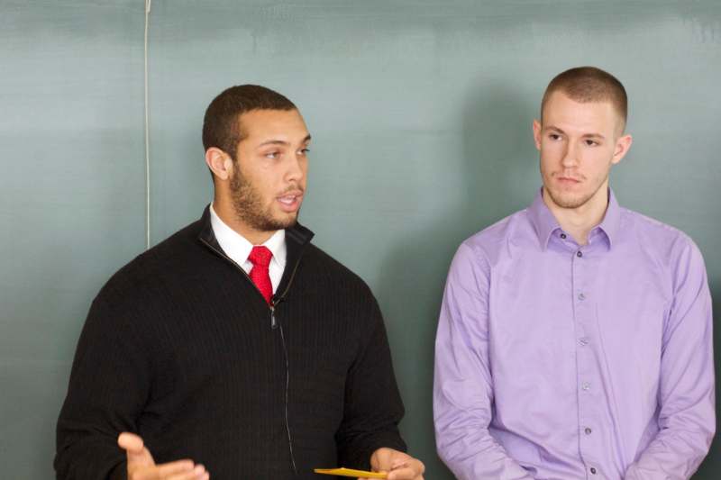 a man in a black sweater and a purple shirt talking to another man