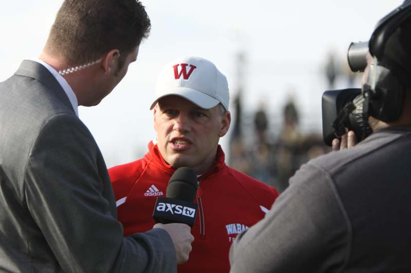 a man in a red jacket talking to a man with microphones