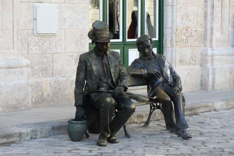 a statue of a man sitting on a bench next to a man sitting on a bench