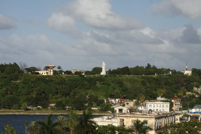 a white statue on a hill with trees and buildings