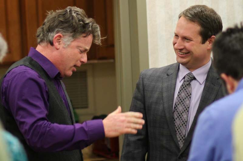 a man in a purple shirt and tie talking to another man