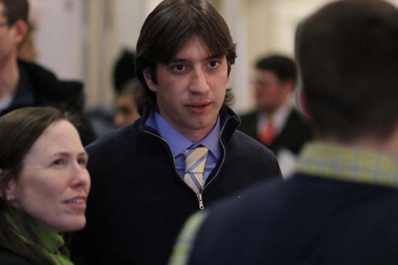 a man in a blue shirt and tie talking to a group of people