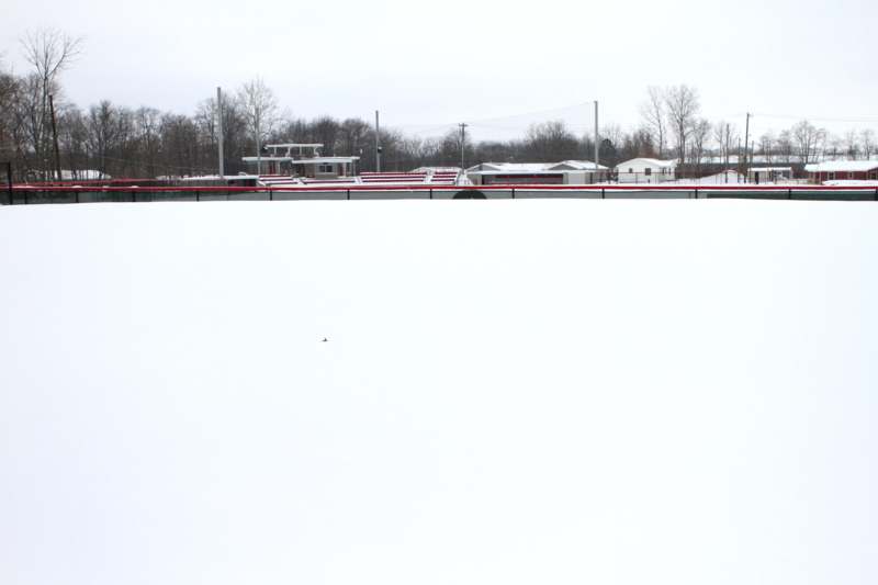a snow covered field with a baseball field and trees