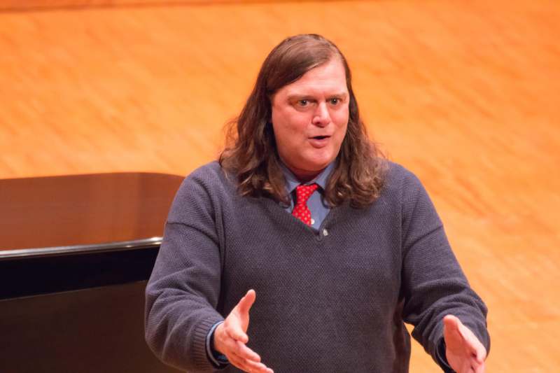 a man with long hair wearing a sweater and red tie