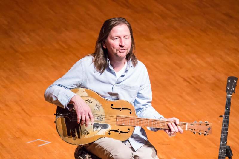 a man sitting on a stage playing a guitar