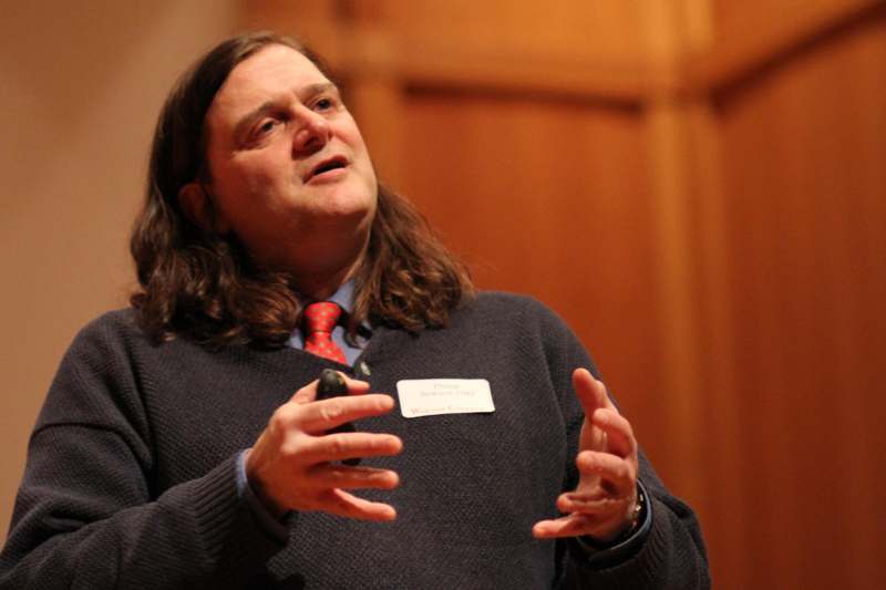 a man with long hair wearing a name tag and a sweater
