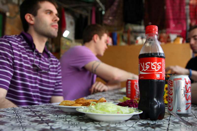 a man sitting at a table with a bottle of soda and food