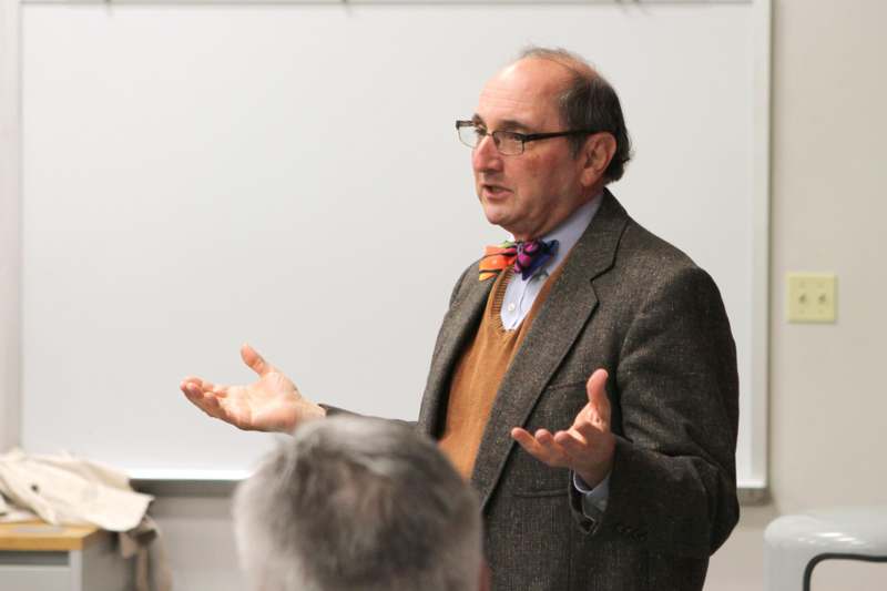 a man in a suit and glasses speaking to a group of people
