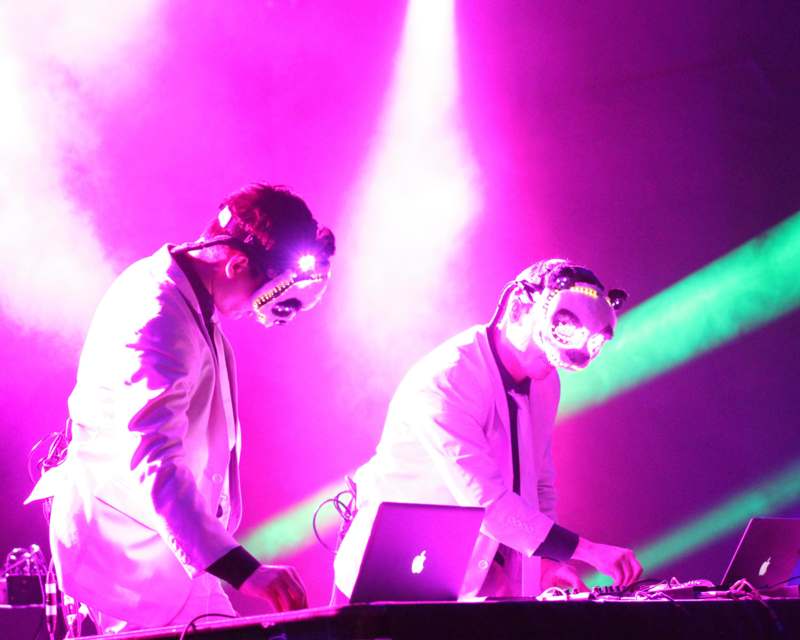 two men wearing masks and a laptop on a stage
