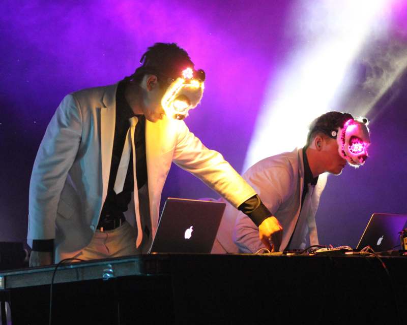 two men wearing masks and standing at a table with laptops
