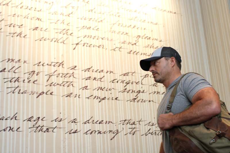 a man in a cap and backpack looking at a large text on a wall