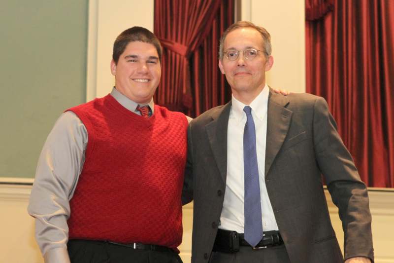 a man in a red vest and tie standing next to another man in a suit