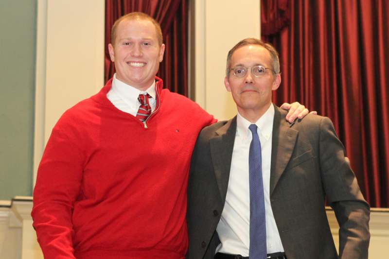 a man in a red sweater and tie standing next to a man in a suit