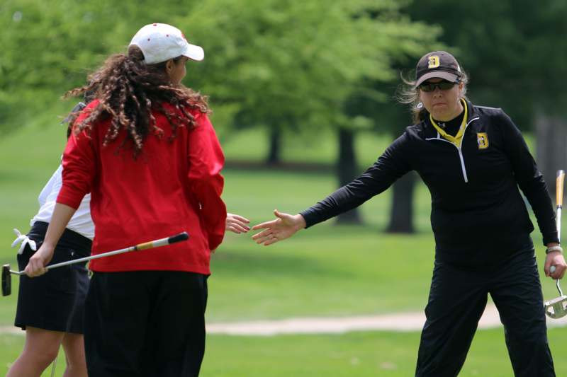 a woman in a black shirt and cap with a golf club in front of another woman