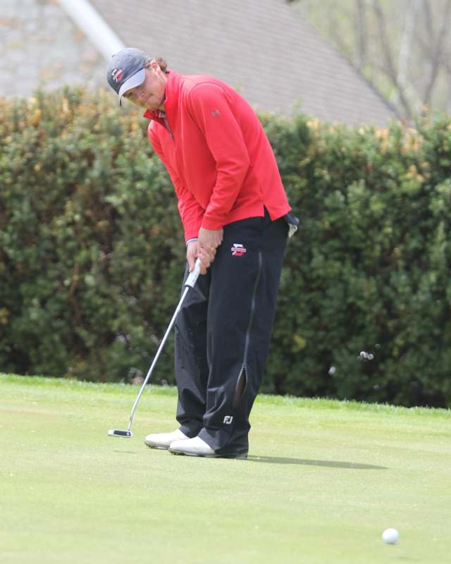 a man in a red shirt and black pants holding a golf club