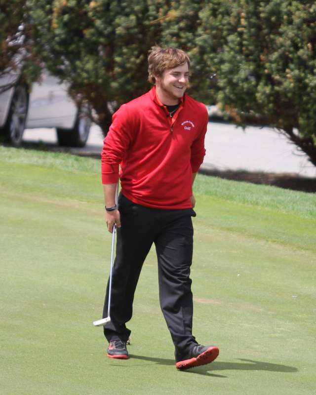 a man in red shirt and black pants holding a golf club