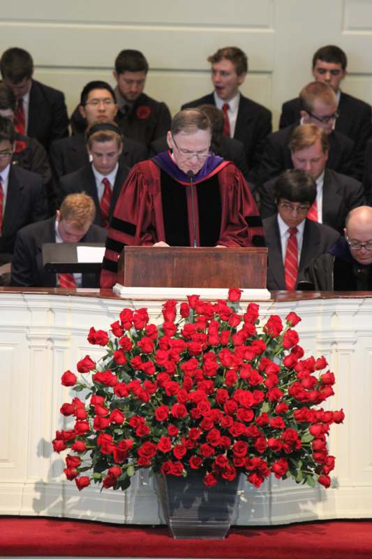 a man in a robe standing at a podium with a large bouquet of roses