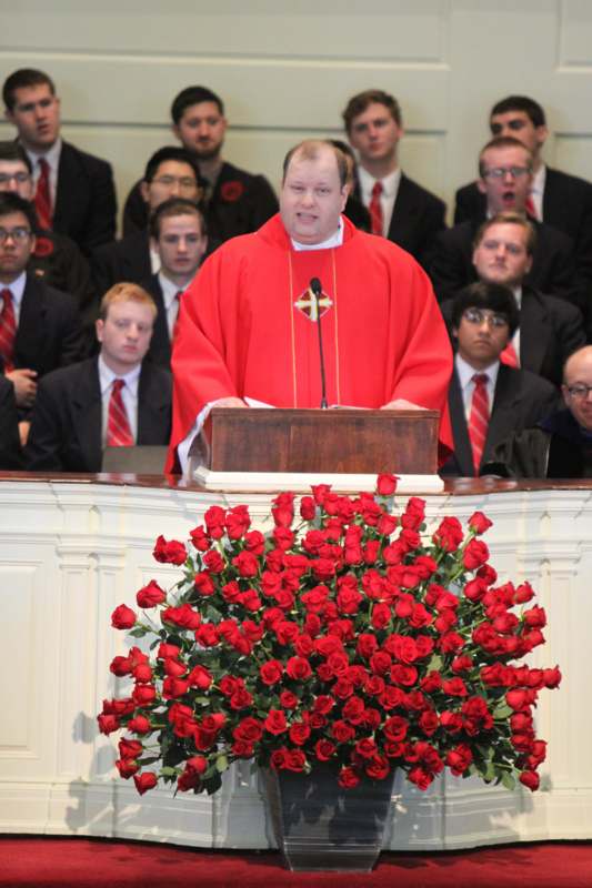 a man in a red robe standing at a podium with a bunch of roses