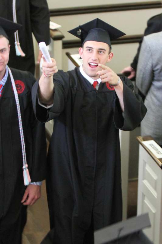 a man in a graduation gown pointing at a diploma