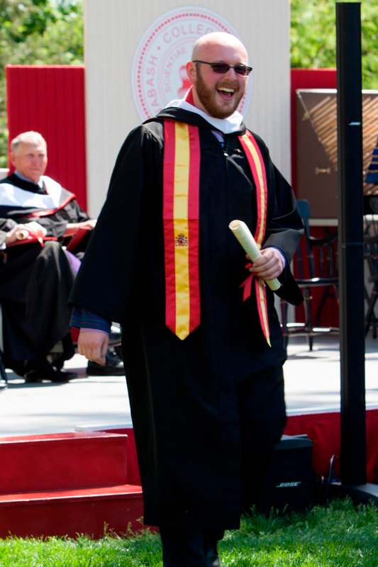a man wearing a graduation gown and holding a diploma