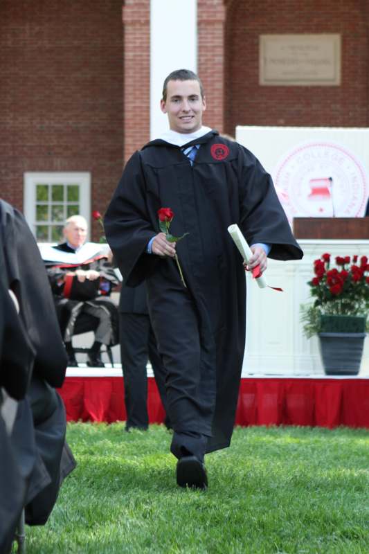 a man in a graduation gown holding a rose and diploma