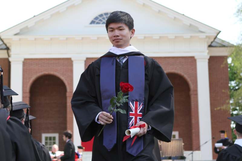 a man in a graduation gown holding a rose and a diploma