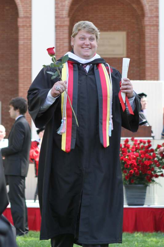 a person in a graduation gown holding a rose