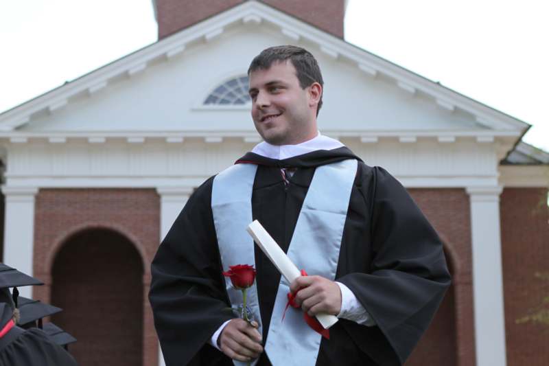 a man in a graduation gown holding a rose and diploma