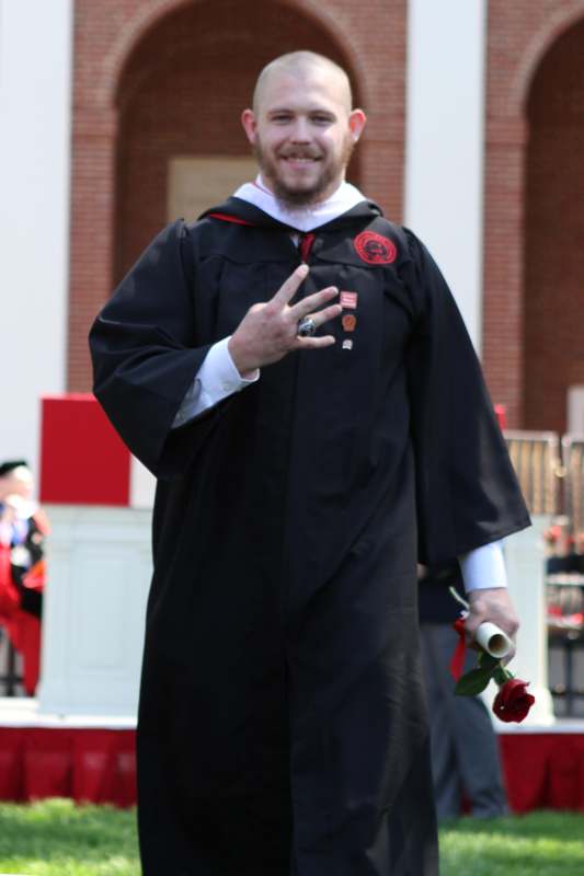 a man in a graduation gown holding a rose and giving the peace sign