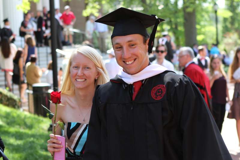 a man in a graduation gown and cap holding a rose
