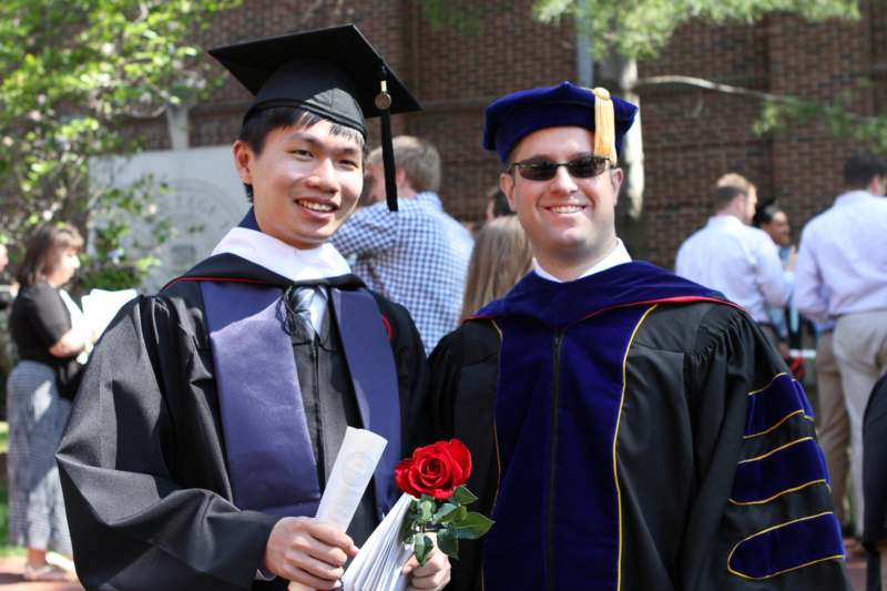 a man in graduation gown and cap holding a rose