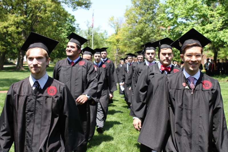 a group of people in graduation gowns and caps walking on grass
