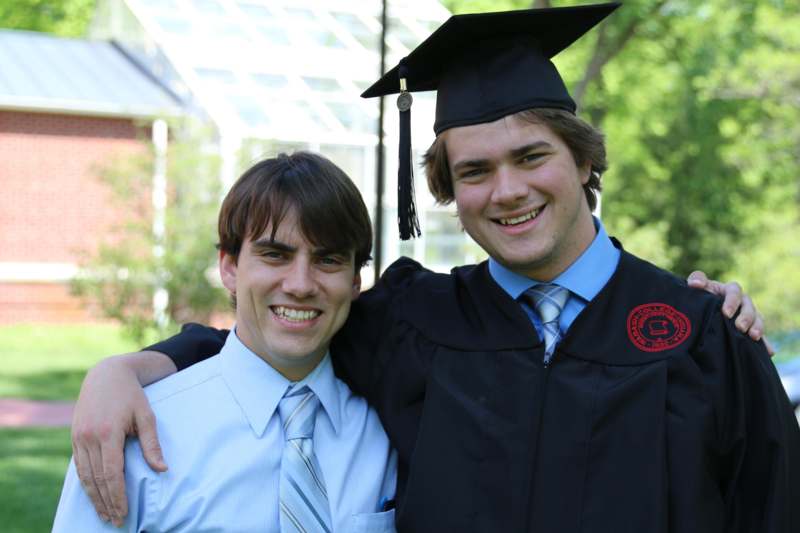 a man in a graduation gown and cap with his arm around another man