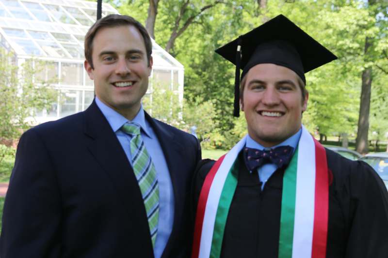 a man in a suit and cap and gown standing next to another man in a graduation cap and gown