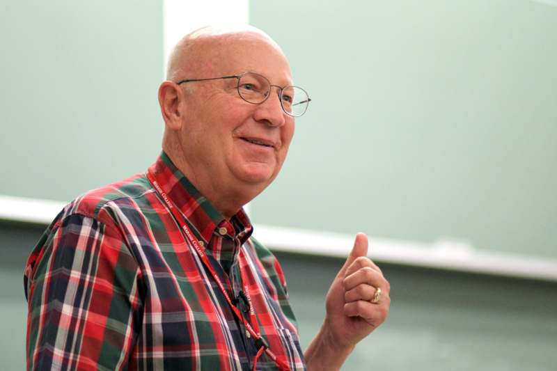 a man wearing glasses and a red and green plaid shirt giving a thumbs up
