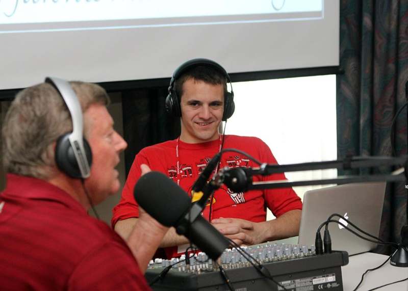 a man wearing headphones and talking to a man in front of a microphone