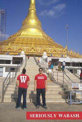 two men standing on stairs in front of a large gold building with Boudhanath in the background