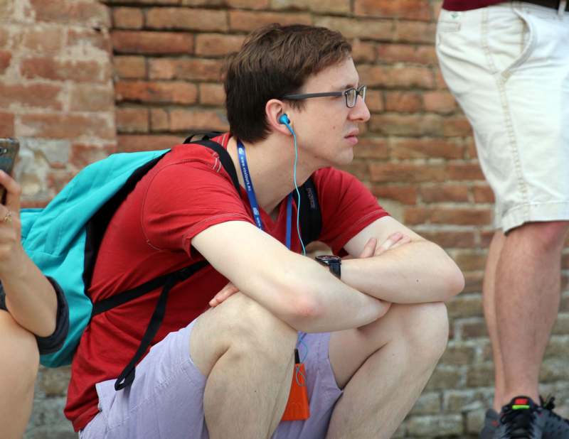 a man wearing glasses and a backpack sitting on the ground